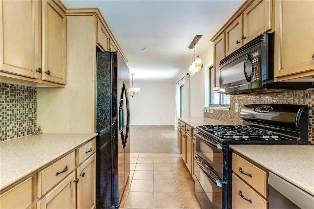 Kitchen featuring warm wood cabinetry with dark hardware, mosaic tile backsplash, black gas range, and black built-in microwave