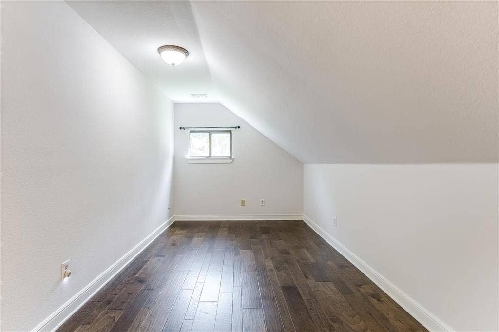 Attic room featuring wood-finish flooring, a window with natural light, and a ceiling-mounted light fixture