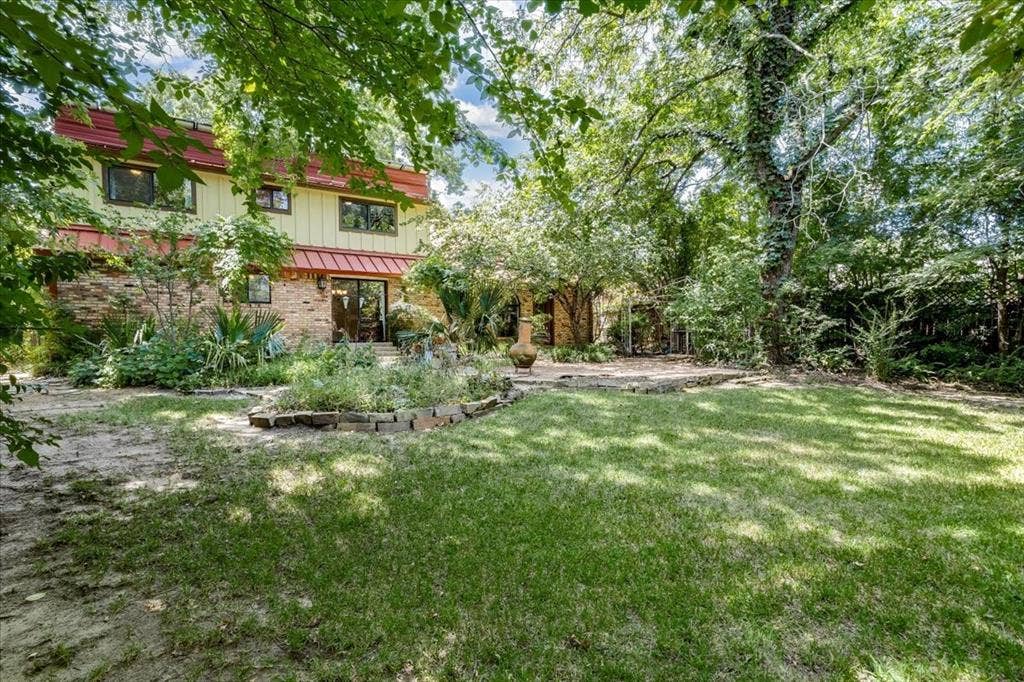 Expansive backyard featuring a manicured lawn, mature trees, and a stone patio