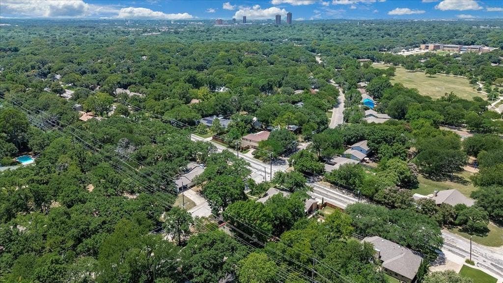 Expansive aerial perspective showcasing a residential area enveloped by mature trees, with a distant urban skyline