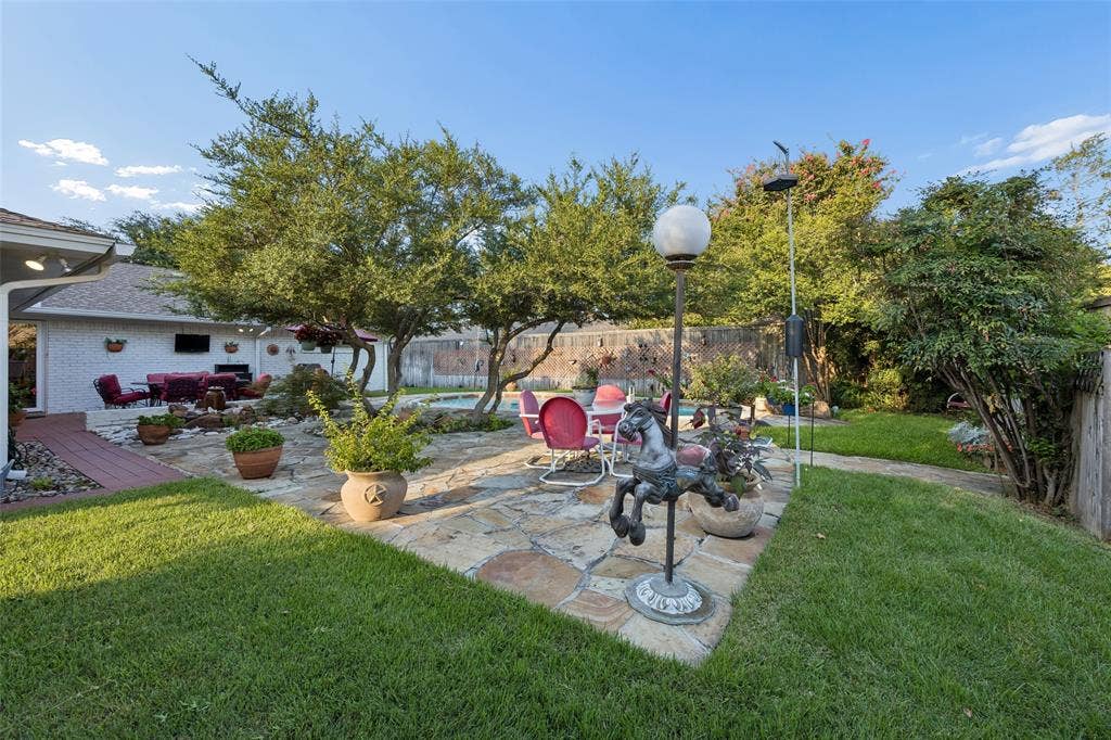 2104 Westlake Drive, Plano, TX 75075 Expansive backyard featuring a stone patio, mature trees, manicured lawn, and a covered outdoor living area with a built-in entertainment system