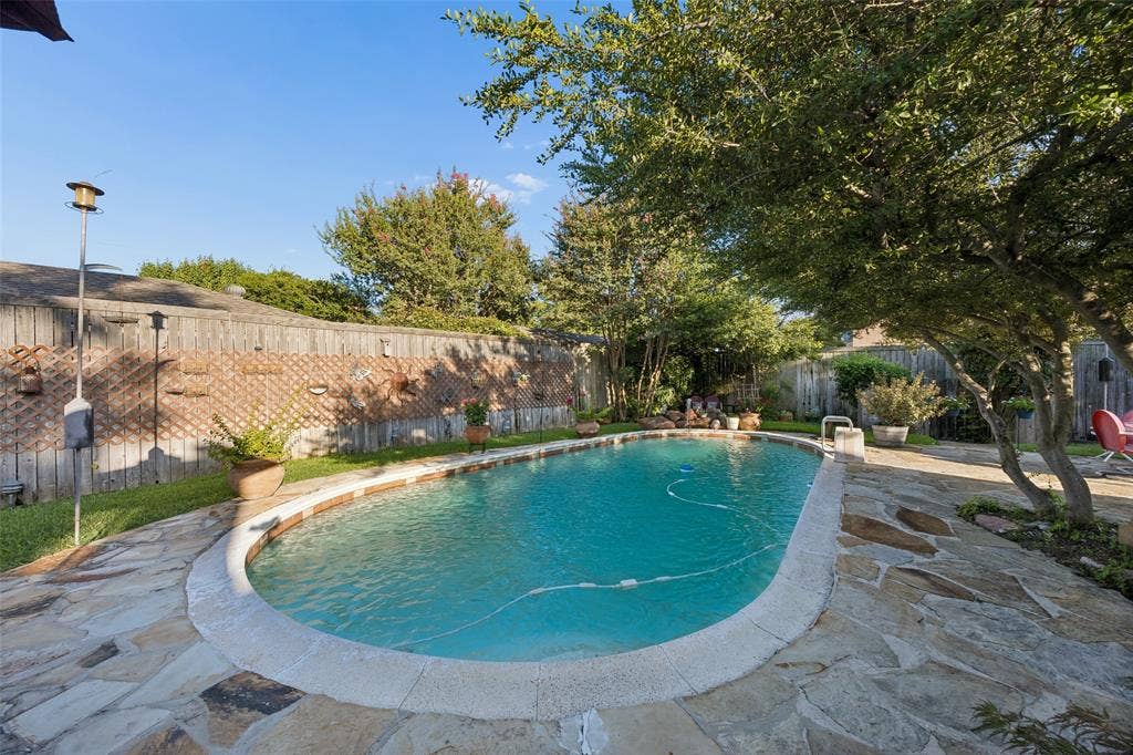 2104 Westlake Drive, Plano, TX 75075 Outdoor swimming pool with flagstone patio surround, perimeter fencing, mature trees, and landscaping