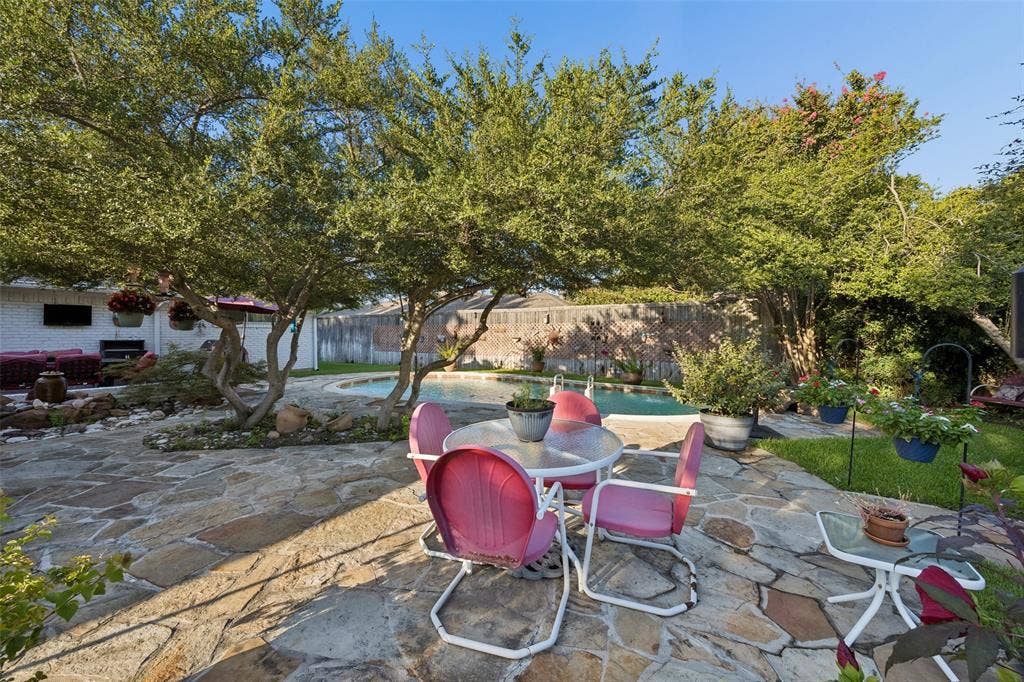 2104 Westlake Drive, Plano, TX 75075 Expansive flagstone patio area with mature trees, a rectangular swimming pool, and a surrounding privacy fence