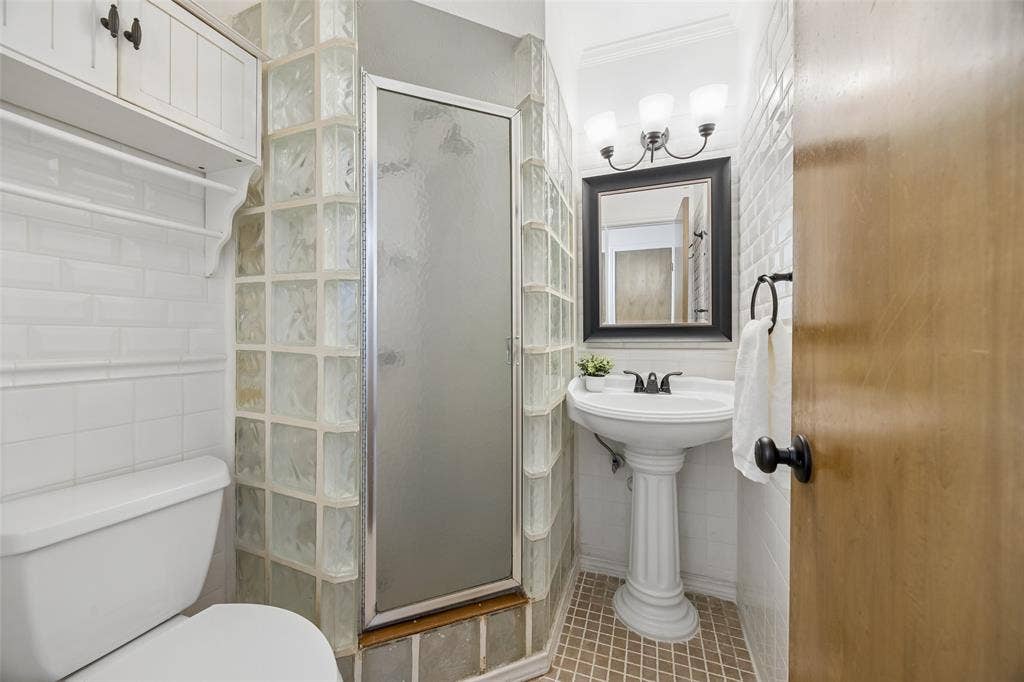 2104 Westlake Drive, Plano, TX 75075 Bathroom featuring a glass block shower enclosure, white subway tile walls, and a pedestal sink with a framed mirror