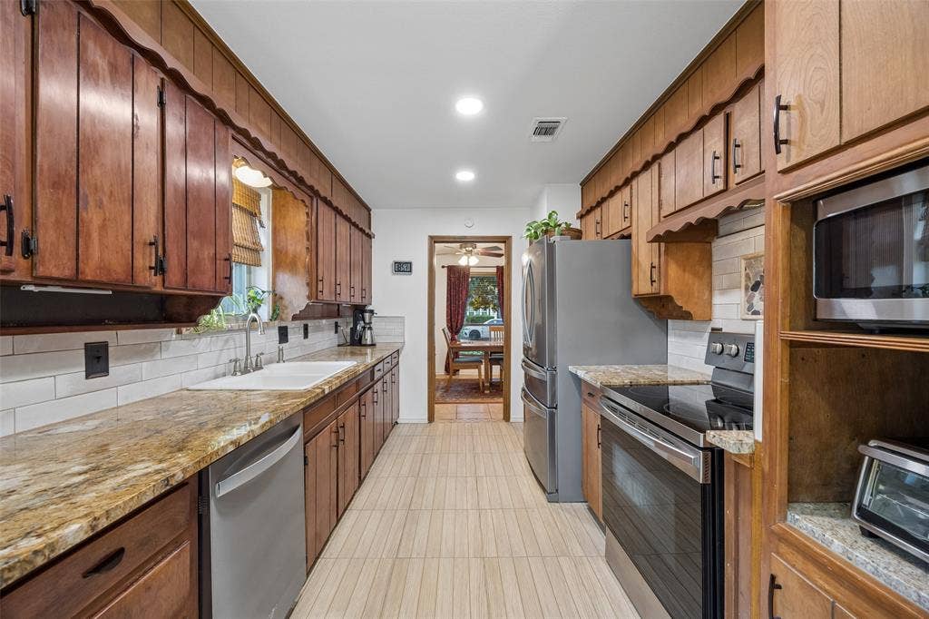 2104 Westlake Drive, Plano, TX 75075 Galley kitchen featuring wood cabinetry, granite-finish countertops, and a white subway tile backsplash