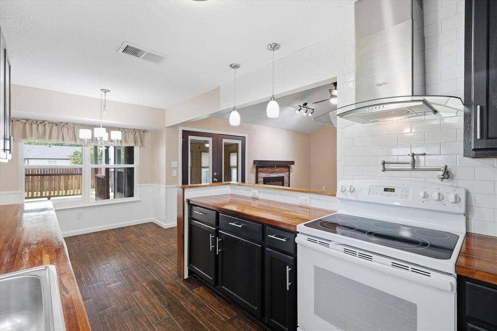 6572 Ridglea Drive, Watauga, TX 76148 Kitchen featuring wood-finish countertops, black cabinetry, white subway tile backsplash, and a modern range hood