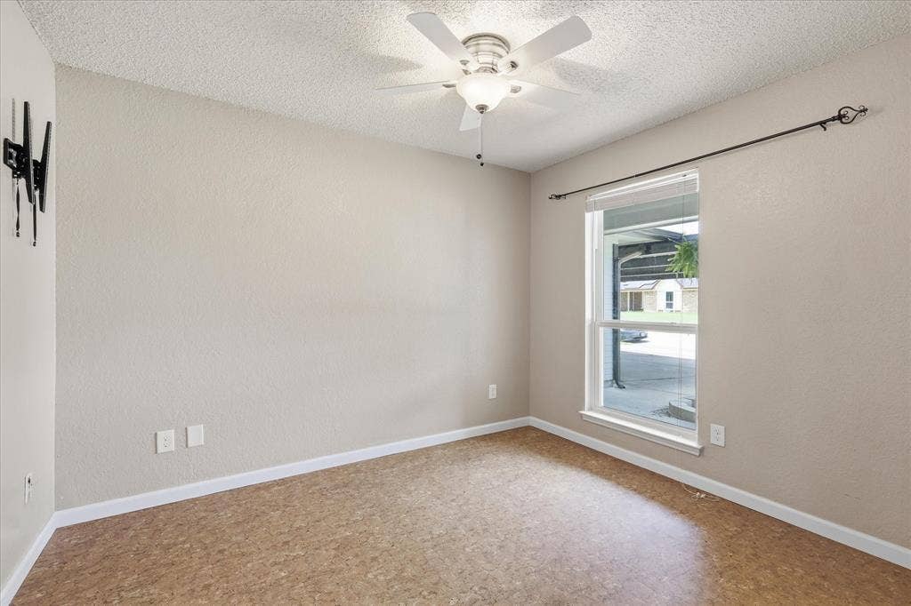 6572 Ridglea Drive, Watauga, TX 76148 Room featuring neutral wall tones, textured ceiling, a window with exterior visibility, wood-finish flooring, and a ceiling fan with integrated lighting