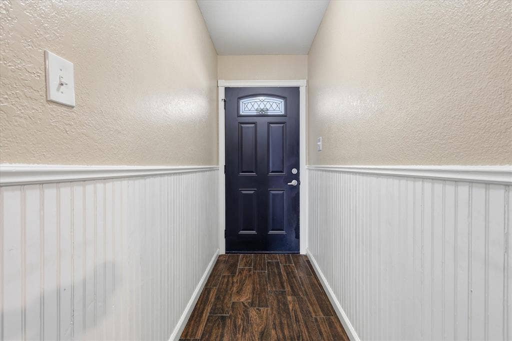 6572 Ridglea Drive, Watauga, TX 76148 Entryway featuring a dark paneled door with decorative glass, wood-finish flooring, and white beadboard wainscoting