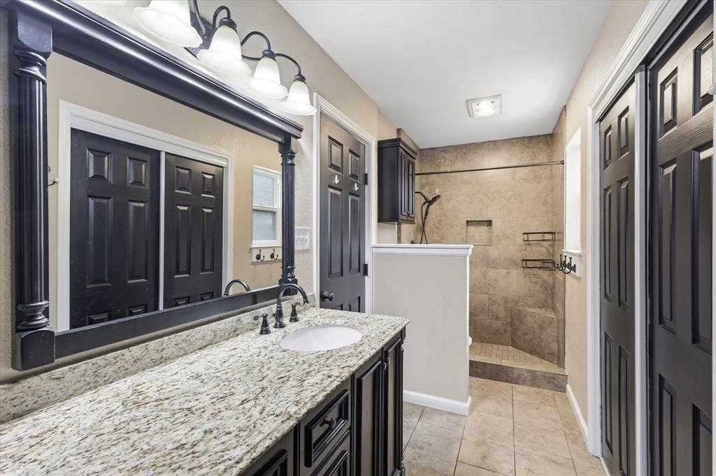 6572 Ridglea Drive, Watauga, TX 76148 Bathroom featuring a vanity with a light-toned speckled countertop, an undermount sink, and dark cabinetry