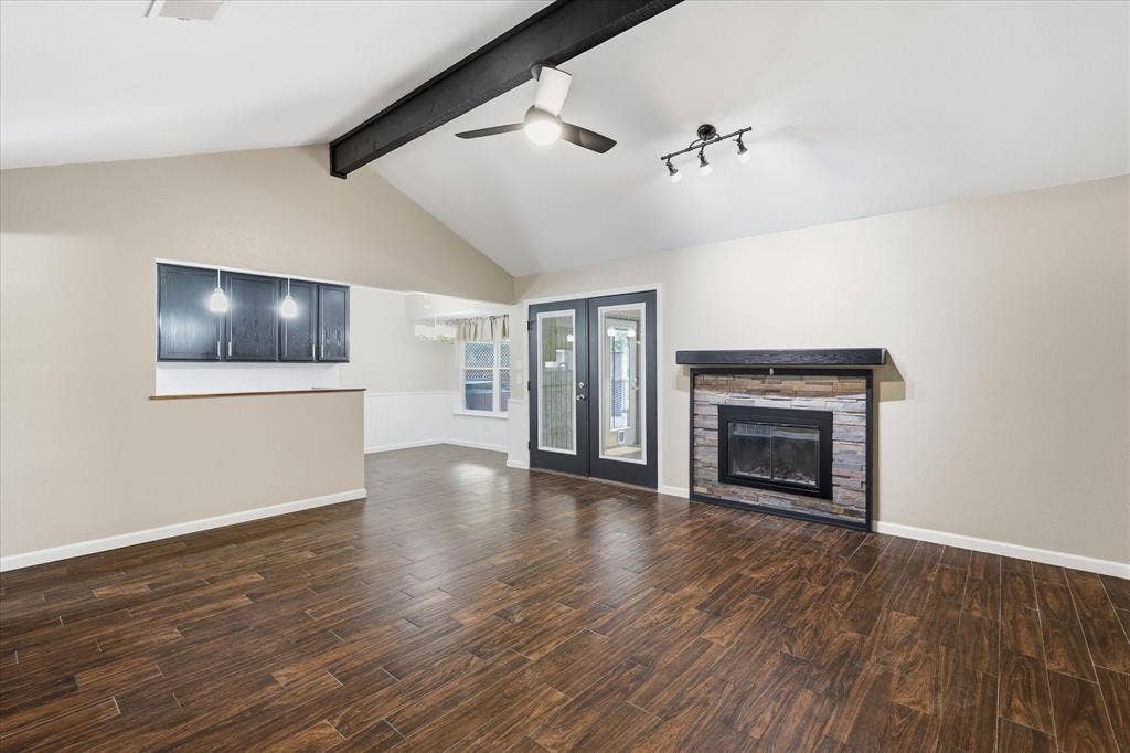 6572 Ridglea Drive, Watauga, TX 76148 Spacious interior featuring wood-finish flooring, a vaulted ceiling with exposed beam, and a stone-accented fireplace