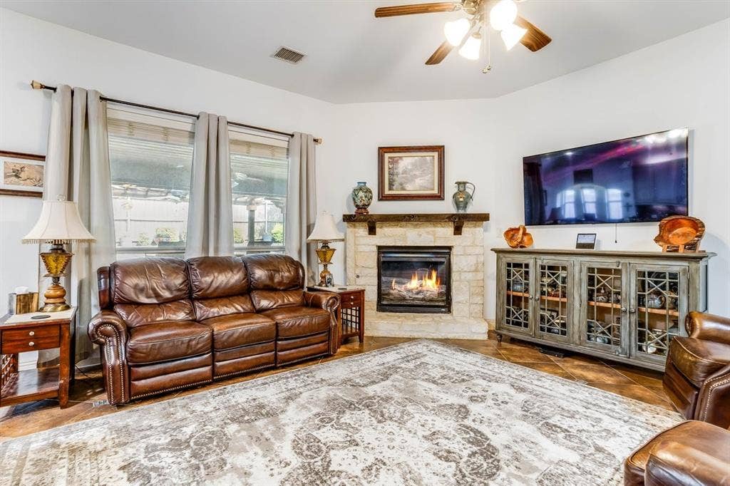 114 Lyndhurst Drive, Wylie, TX 75098 Living area featuring tile flooring, a stone-faced fireplace with a wood mantle, and a ceiling fan with integrated lighting
