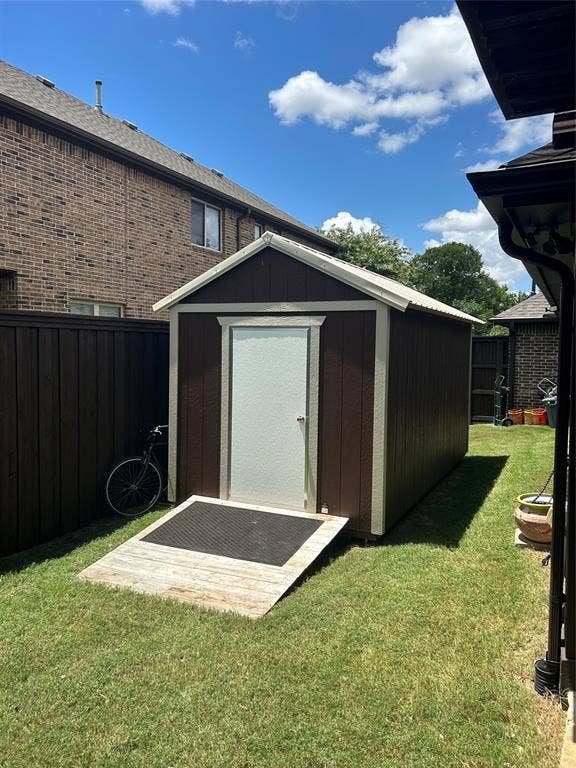 114 Lyndhurst Drive, Wylie, TX 75098 Detached storage shed with brown siding and white trim, featuring a white door, a sloped wood ramp, and a metal roof