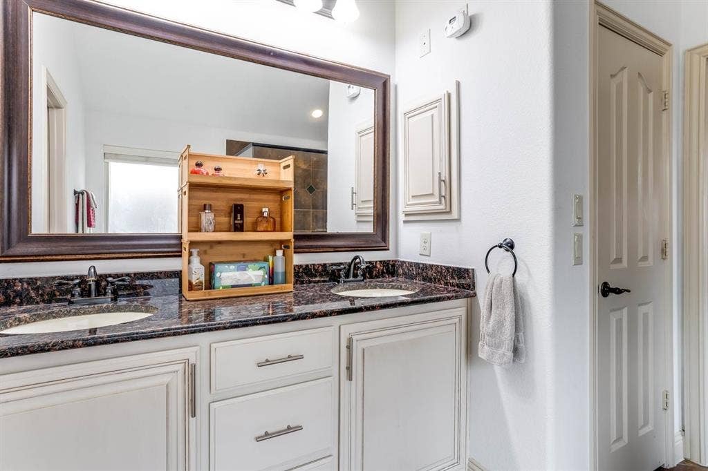 114 Lyndhurst Drive, Wylie, TX 75098 Double vanity with under-mount sinks, dark stone countertop, and custom white cabinetry
