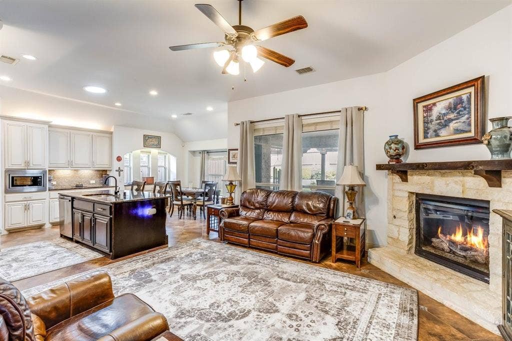 114 Lyndhurst Drive, Wylie, TX 75098 Open-concept living space featuring wood-finish flooring, a stone-surround fireplace with a wood mantel, and an overhead ceiling fan