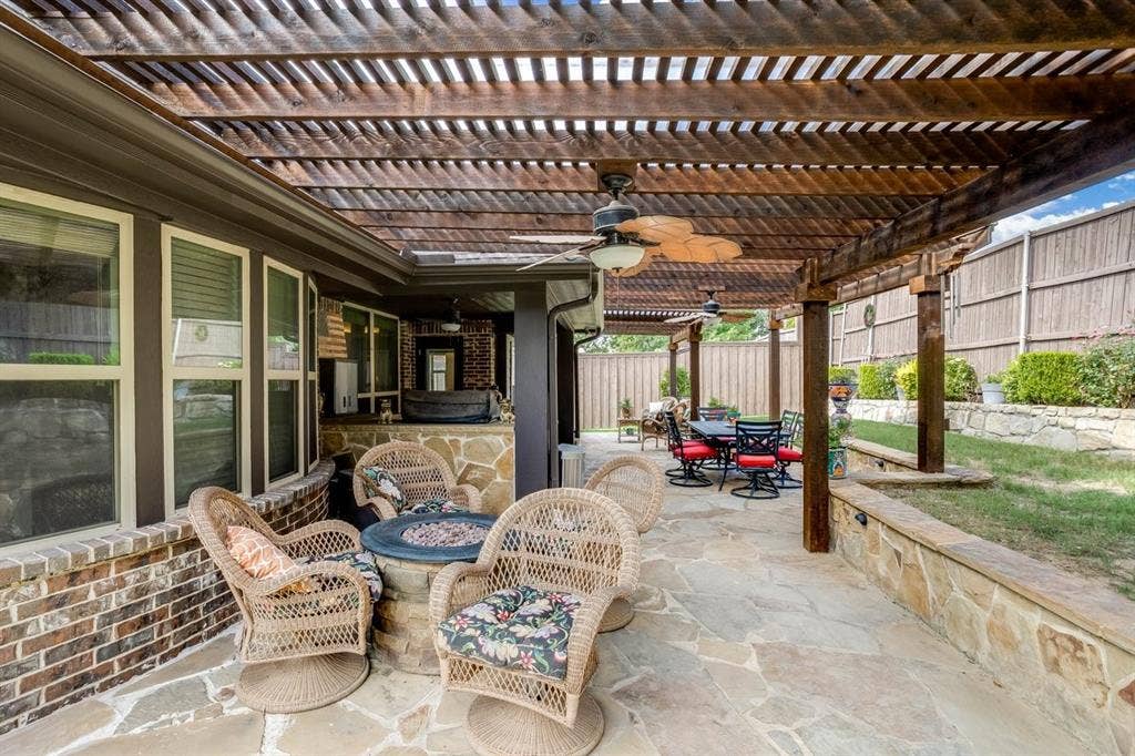 114 Lyndhurst Drive, Wylie, TX 75098 Expansive stone patio with a wood pergola, integrated ceiling fans, and a built-in fire pit