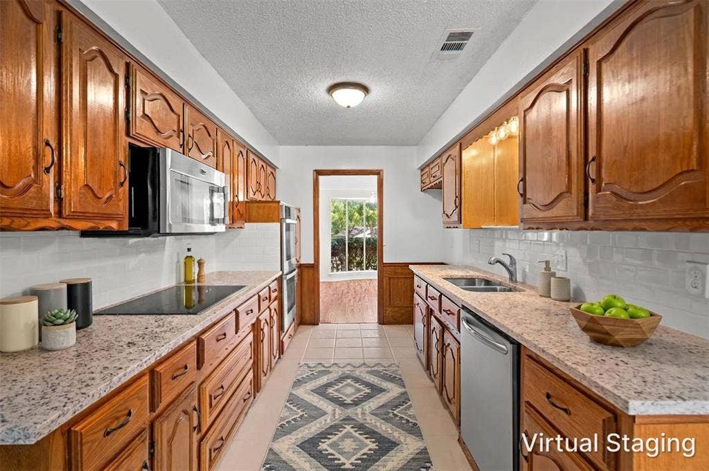 1315 Winding Brook Drive, DeSoto, TX 75115 Galley kitchen featuring wood cabinetry, stone-finish countertops, stainless steel appliances, a tile backsplash, and recessed lighting