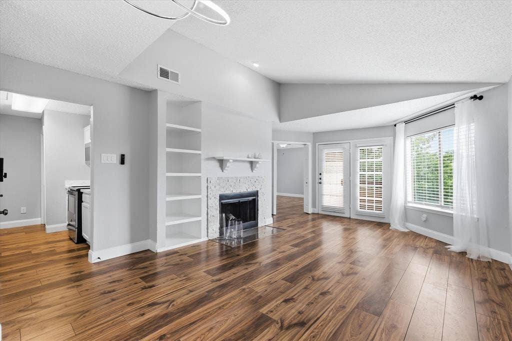 5550 Spring Valley Road, #A31, Dallas, TX 75254 Spacious living area featuring wood-finish flooring, a fireplace with a mosaic tile surround, and built-in shelving