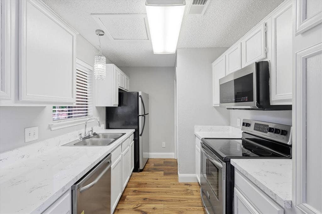 5550 Spring Valley Road, #A31, Dallas, TX 75254 Modern galley kitchen featuring white cabinetry, light countertops, wood-finish flooring, and stainless steel appliances including a built-in microwave and dishwasher