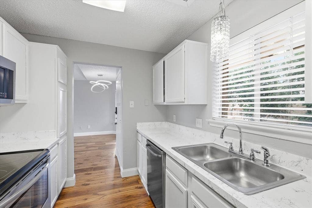 5550 Spring Valley Road, #A31, Dallas, TX 75254 Galley-style kitchen featuring white cabinetry, light-toned countertops, a dual-basin stainless steel sink with a chrome faucet, and wood-finish flooring