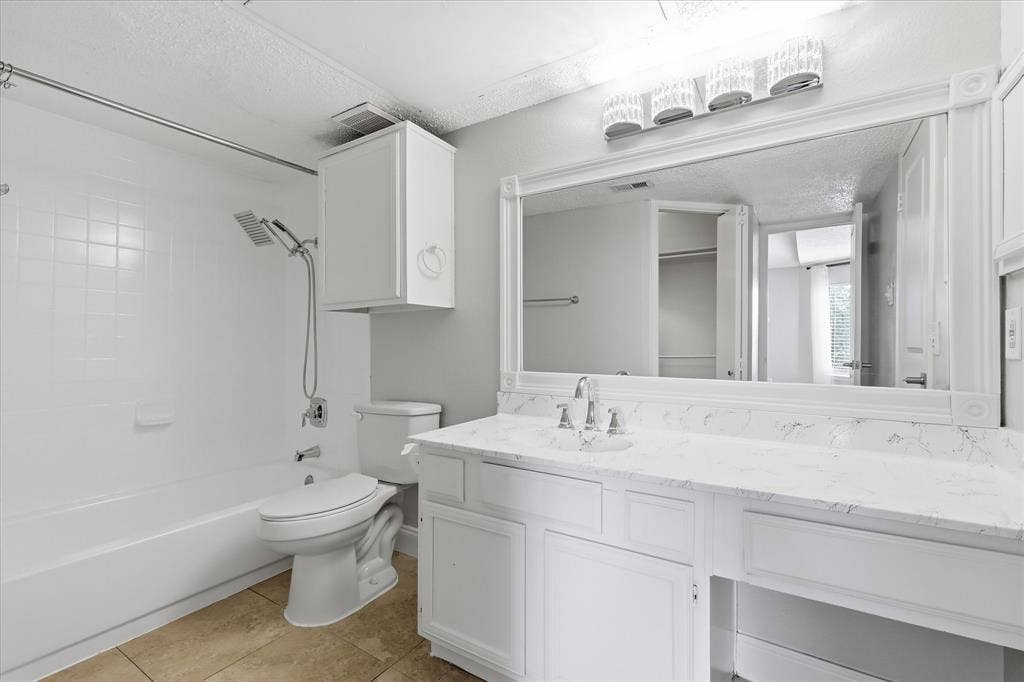 5550 Spring Valley Road, #A31, Dallas, TX 75254 Bathroom featuring a vanity with a white countertop and integrated sink, a large wall-mounted mirror, white shaker-style cabinetry, and a tub/shower combination with white subway tile surround