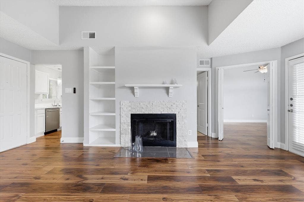 5550 Spring Valley Road, #A31, Dallas, TX 75254 Living area featuring a fireplace with a textured stone surround, wood-finish flooring, and built-in shelving