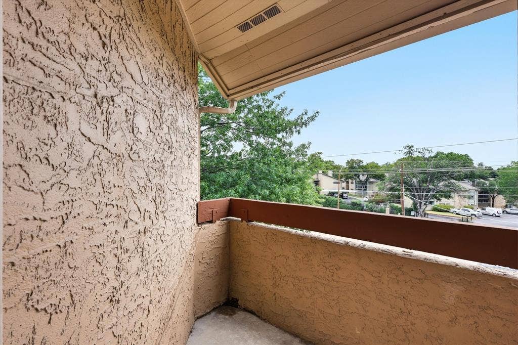 5550 Spring Valley Road, #A31, Dallas, TX 75254 Private outdoor balcony with textured stucco walls, wood-finish railing, and a clear sky overhead