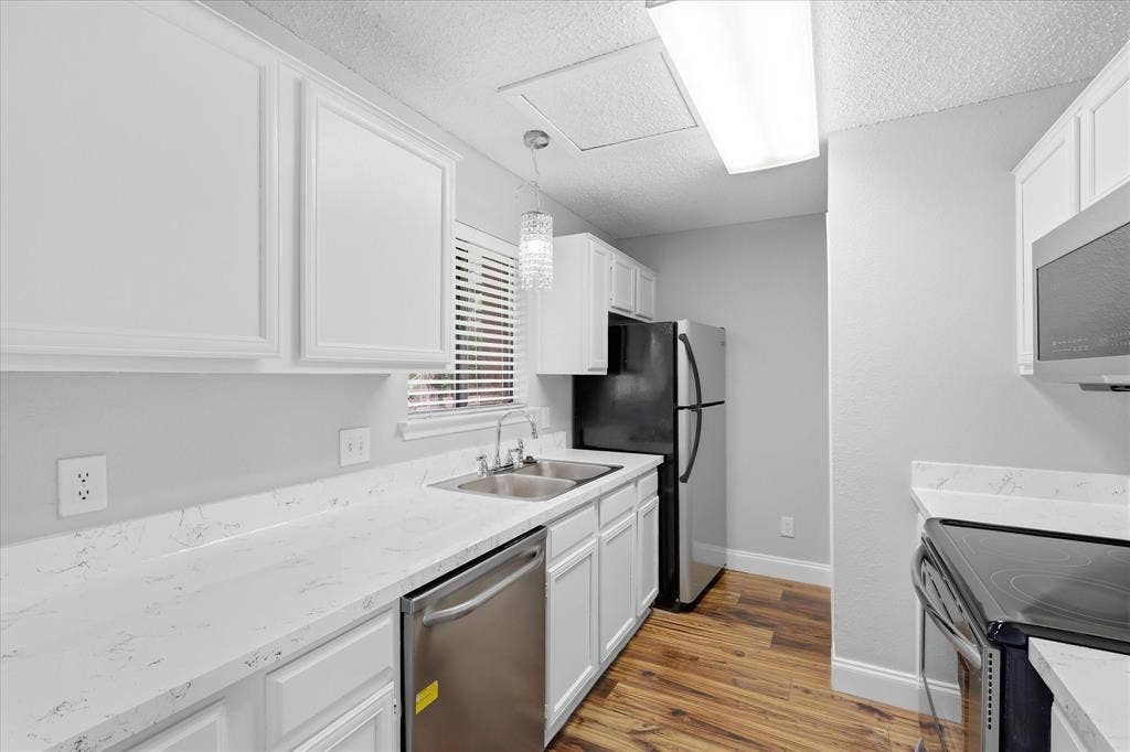 5550 Spring Valley Road, #A31, Dallas, TX 75254 Kitchen featuring white cabinetry, light-colored countertops, stainless steel appliances, and wood-finish flooring