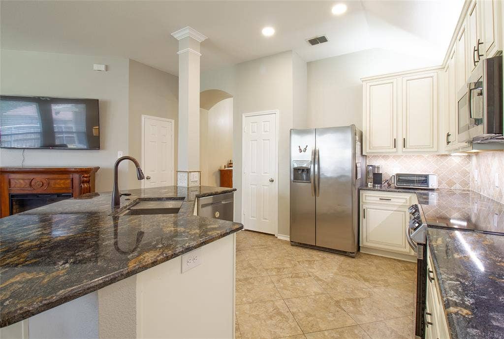 406 Hackberry Drive, Fate, TX 75087 Kitchen featuring dark granite countertops, cream cabinetry with dark hardware, a stainless steel refrigerator, and tiled flooring