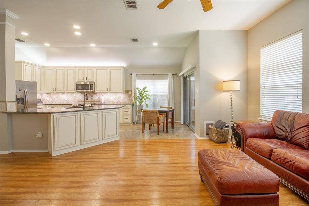 406 Hackberry Drive, Fate, TX 75087 Open-concept living area featuring wood-finish flooring, a kitchen with off-white cabinetry, dark countertops, and stainless steel appliances, and a dining area with tile flooring
