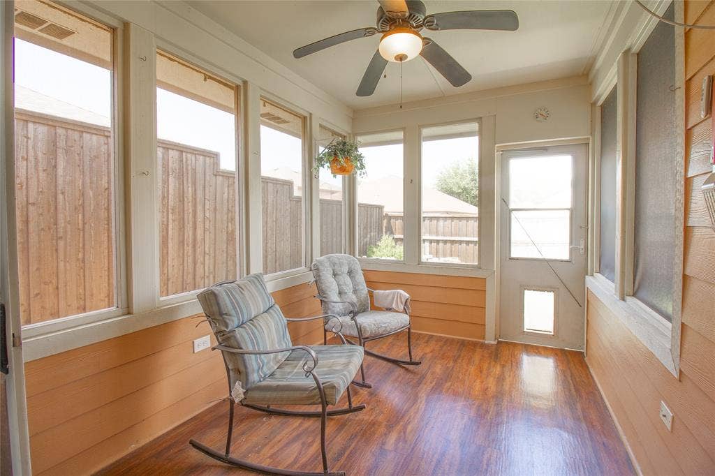 406 Hackberry Drive, Fate, TX 75087 Enclosed sunroom featuring multiple large windows, wood-finish flooring, a ceiling fan with integrated lighting, and a rear door with a lower pet entrance