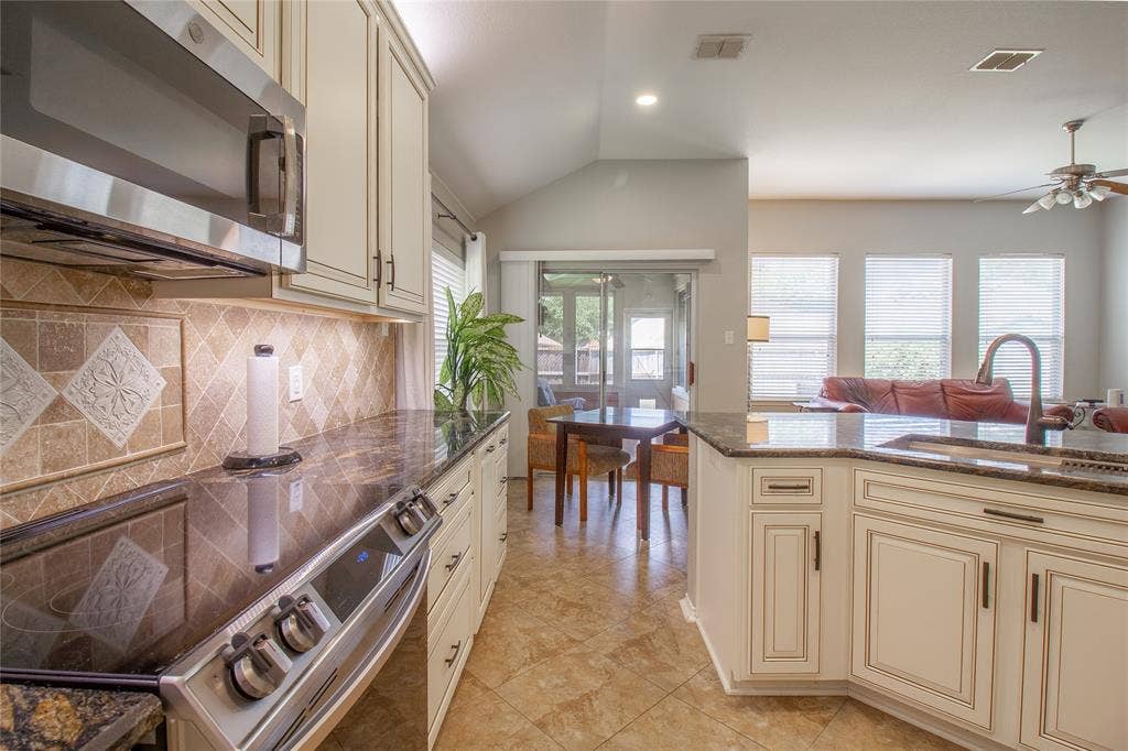 406 Hackberry Drive, Fate, TX 75087 Kitchen featuring stainless steel appliances, granite countertops, tile backsplash, cream cabinetry, and tile flooring