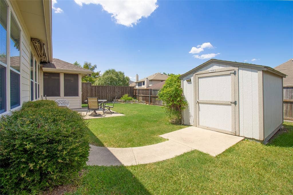 406 Hackberry Drive, Fate, TX 75087 Expansive backyard featuring a lush lawn, concrete patio, privacy fencing, and a detached storage shed