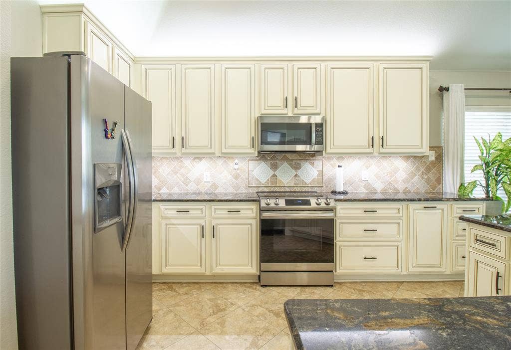 406 Hackberry Drive, Fate, TX 75087 Kitchen featuring cream-colored cabinetry, stainless steel appliances, dark stone countertops, and a patterned tile backsplash