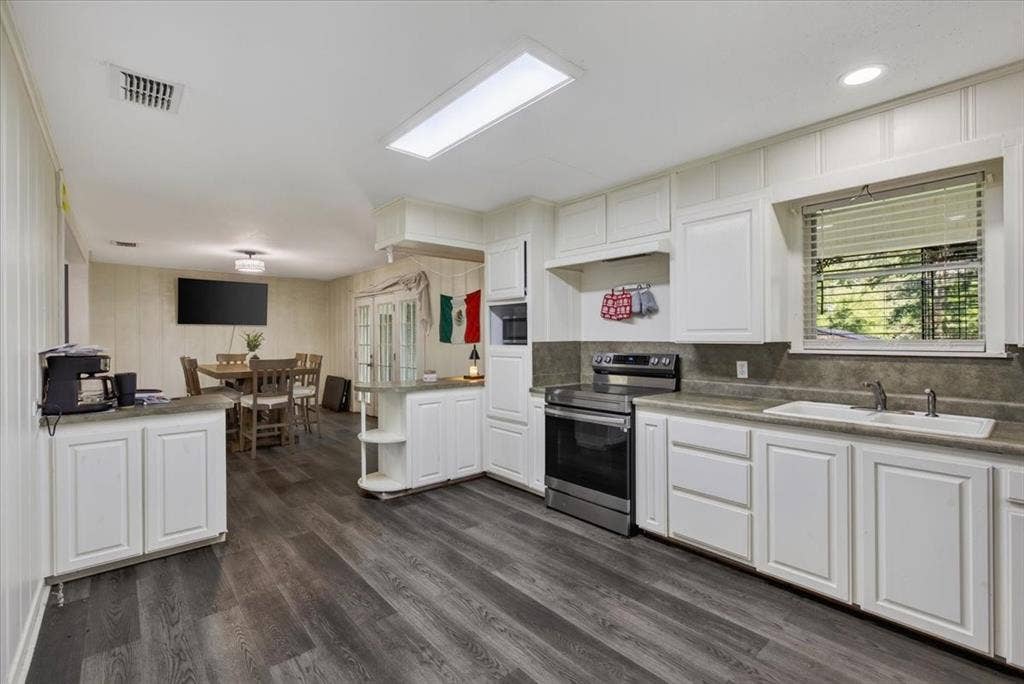 925 Maryland Drive, Athens, TX 75751 Open-concept kitchen featuring wood-finish flooring, white cabinetry, a built-in microwave, and a stainless steel range