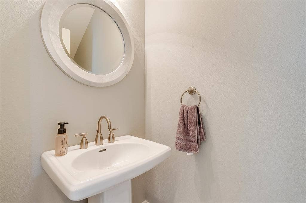 1211 S Adams Street, Fort Worth, TX 76104 Pedestal sink with brushed nickel faucet, complemented by a circular framed mirror and towel ring