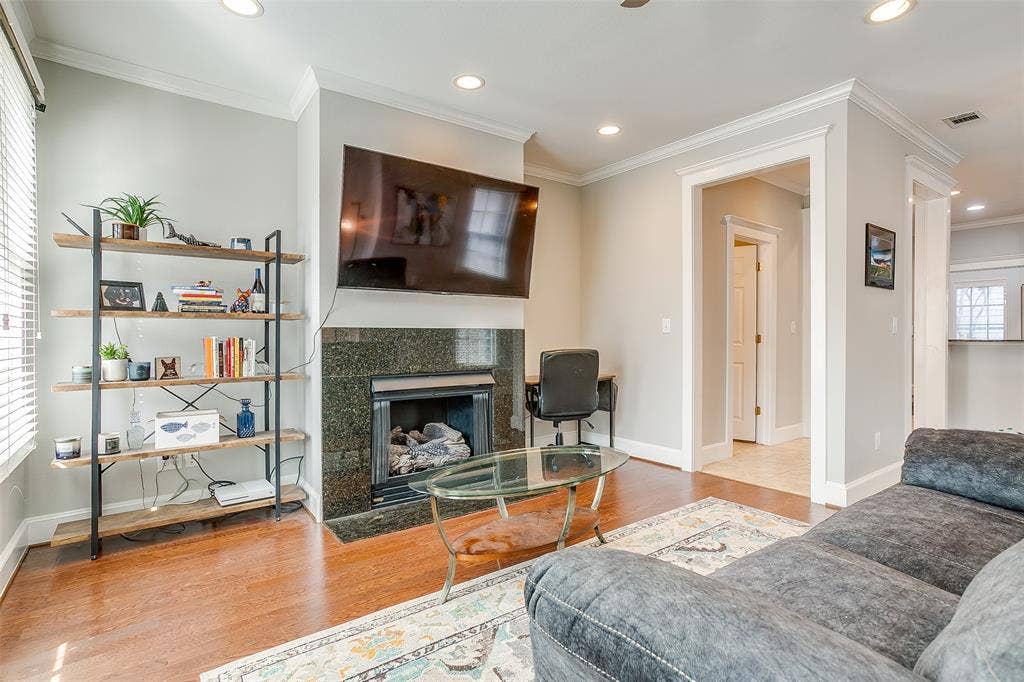 1211 S Adams Street, Fort Worth, TX 76104 Living area featuring a fireplace with a dark stone surround, wood-finish flooring, recessed lighting, crown molding, and bright white trim