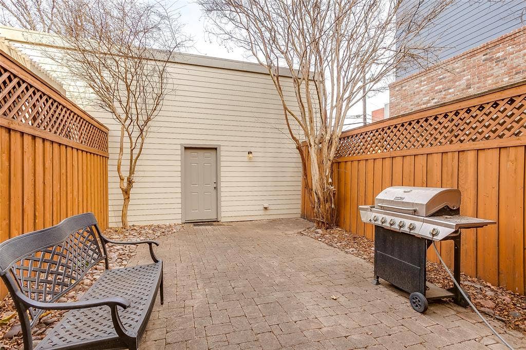 1211 S Adams Street, Fort Worth, TX 76104 Private paver patio featuring a full-height wooden fence with lattice detailing, a separate exterior door, and a gravel border