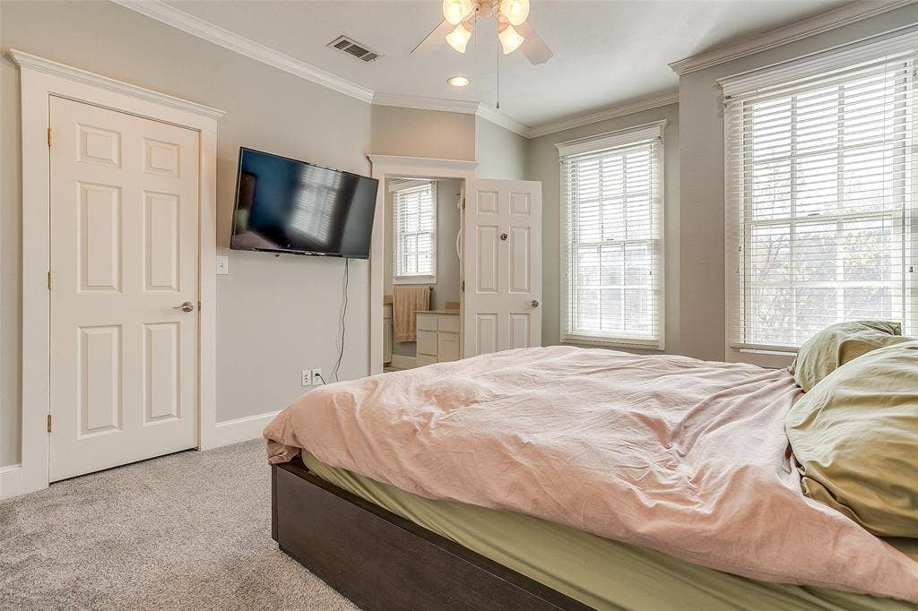 1211 S Adams Street, Fort Worth, TX 76104 Carpeted room featuring two prominent windows with blinds, a ceiling fan with integrated lighting, and a six-panel interior door