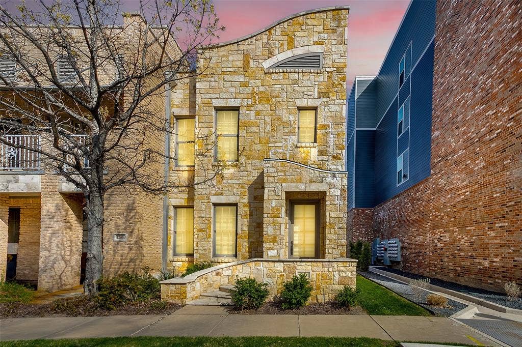 1211 S Adams Street, Fort Worth, TX 76104 Stone facade residence featuring a unique curved roofline, multiple window openings, and a stone-clad entry with steps