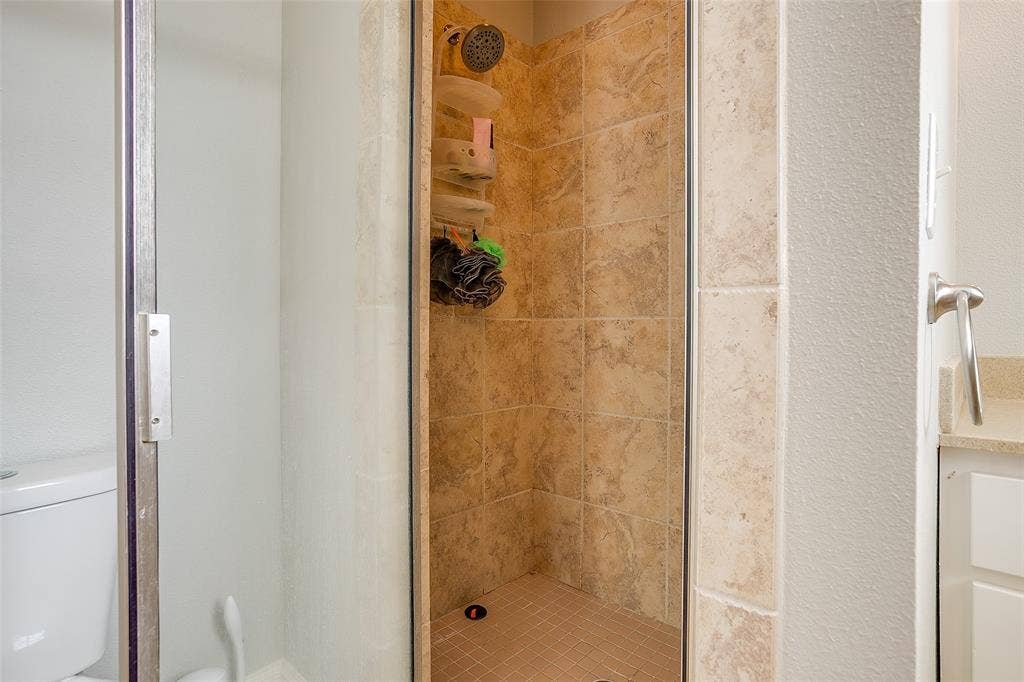 1211 S Adams Street, Fort Worth, TX 76104 Walk-in shower featuring natural-toned tile surround and a coordinating tiled floor