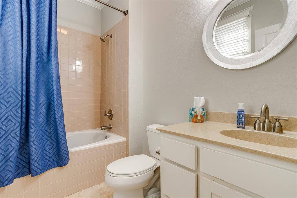 1211 S Adams Street, Fort Worth, TX 76104 Bathroom featuring a built-in bathtub with light-toned wall tile, a white vanity with under-sink cabinetry, a light-toned countertop with an integrated sink, and a framed oval mirror