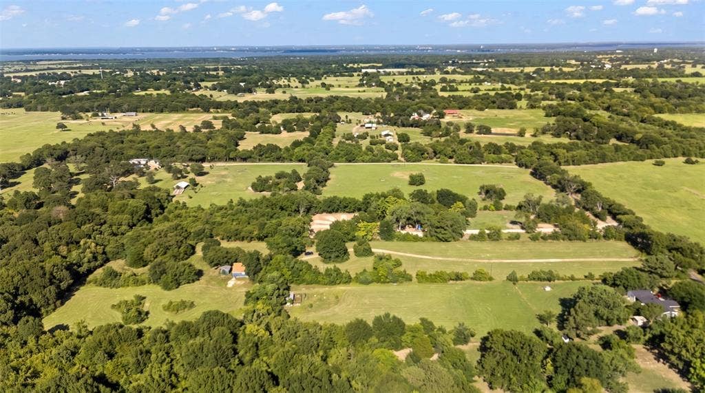 28300 County Road 2100, Kemp, TX 75143 Expansive rural landscape featuring extensive green pastures, abundant mature trees, multiple agricultural structures, and a distant body of water