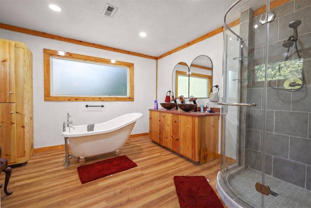 28300 County Road 2100, Kemp, TX 75143 Spacious bathroom featuring a freestanding clawfoot tub, a dual vanity with vessel sinks, a glass-enclosed shower, wood-finish flooring, and natural wood trim accents