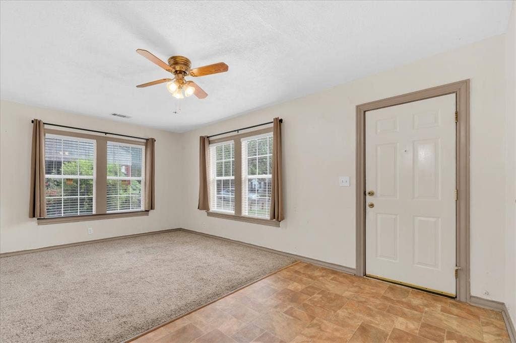 1113 Hudgins Avenue, Fort Worth, TX 76111 Living area featuring a ceiling fan with integrated lighting, two windows with blinds and curtain rods, and neutral-toned wall-to-wall carpeting