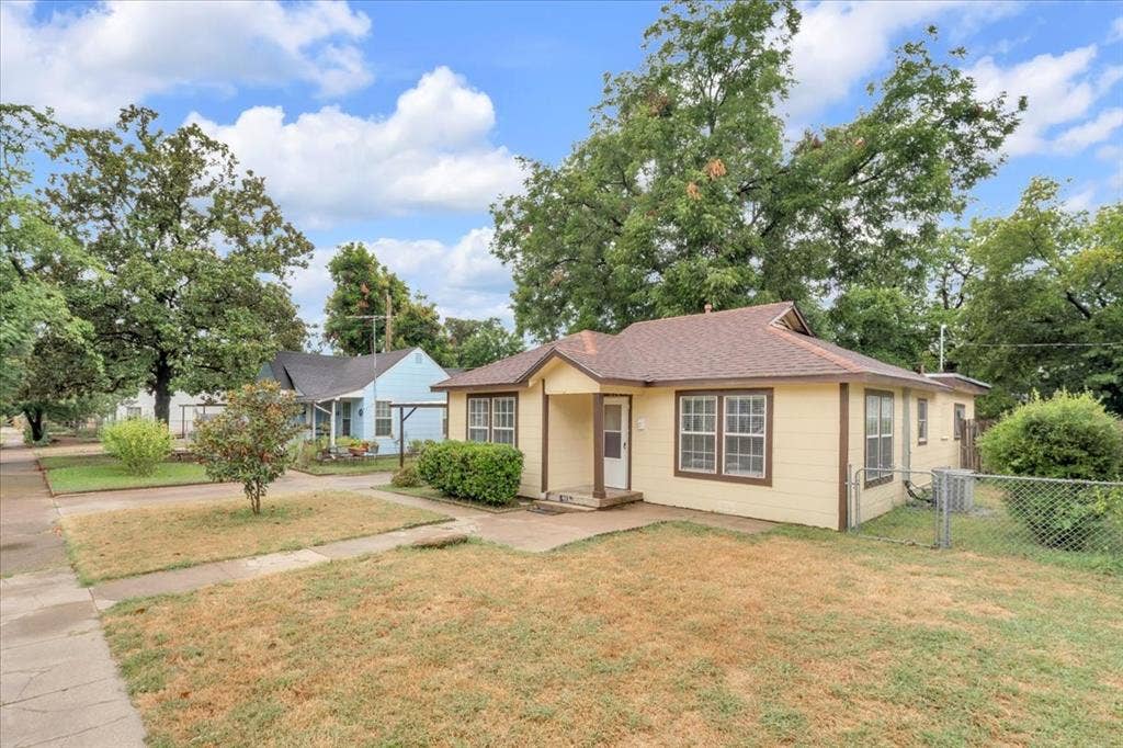 1113 Hudgins Avenue, Fort Worth, TX 76111 Single-story residence featuring a yellow exterior with brown trim, a brown shingle roof, and multiple pane windows