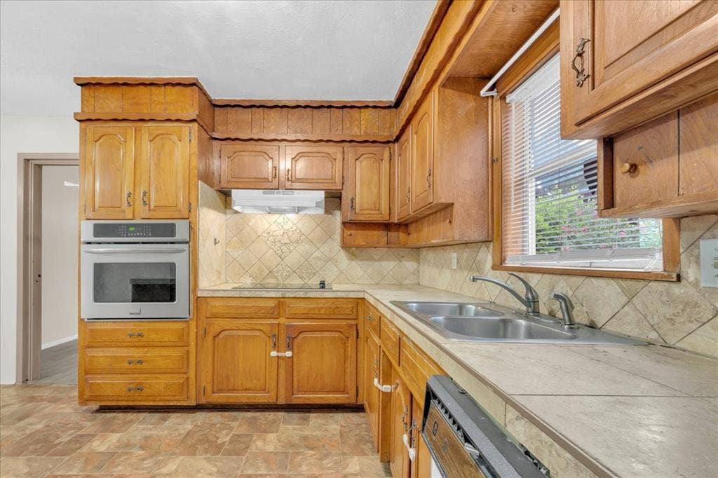 1113 Hudgins Avenue, Fort Worth, TX 76111 Kitchen featuring wood cabinetry, stainless steel wall oven, tile countertops, tile backsplash, and a double basin stainless steel sink