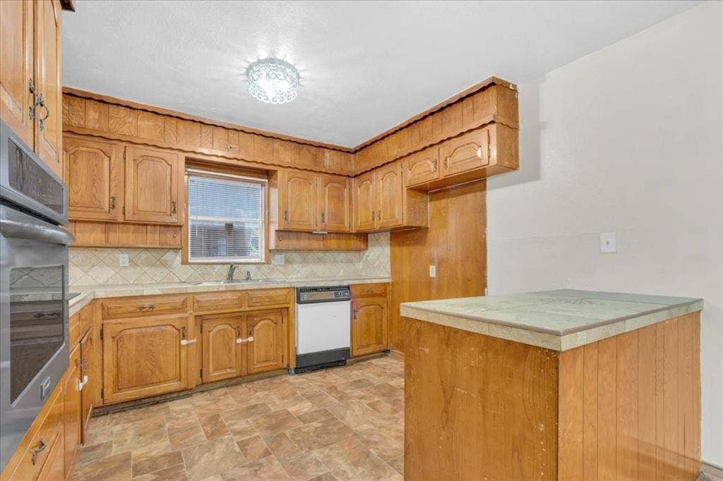 1113 Hudgins Avenue, Fort Worth, TX 76111 Kitchen featuring wood cabinetry, a built-in oven and microwave, a dishwasher, and a window above the sink