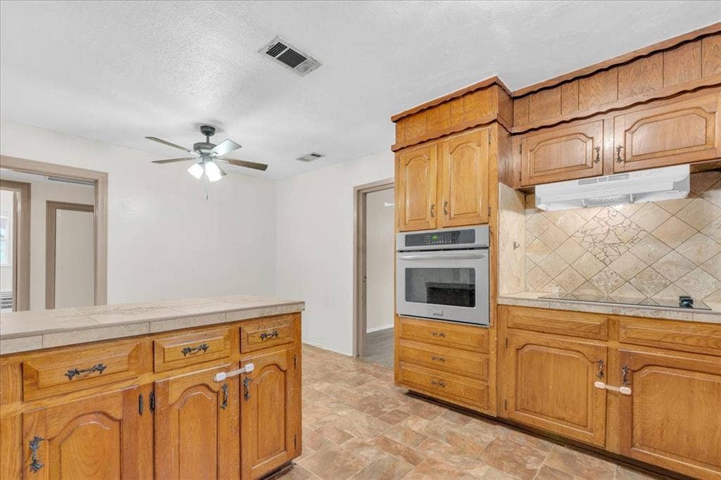 1113 Hudgins Avenue, Fort Worth, TX 76111 Kitchen featuring wood cabinetry, tile countertops, built-in stainless steel oven, and a patterned tile backsplash