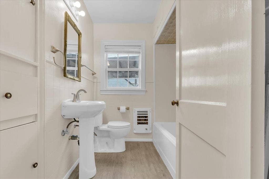 1113 Hudgins Avenue, Fort Worth, TX 76111 Bathroom featuring a pedestal sink, a window, built-in cabinetry, a toilet, and a bathtub