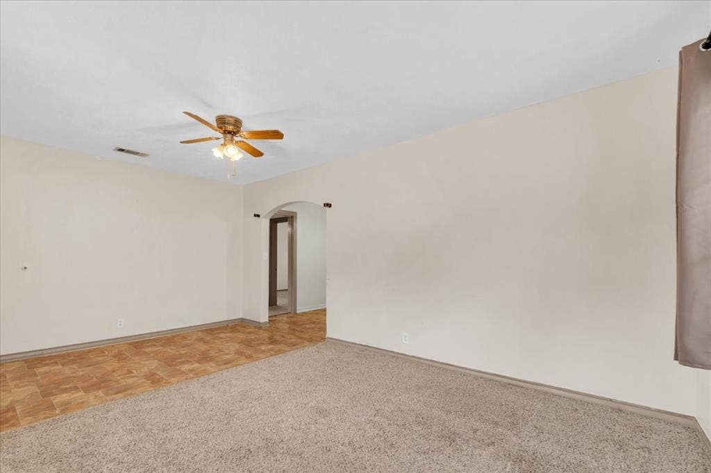 1113 Hudgins Avenue, Fort Worth, TX 76111 Spacious interior room featuring a ceiling fan with integrated lighting, a broad arched doorway, and a combination of neutral-toned carpeting and wood-finish flooring